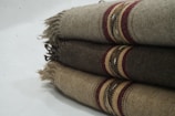 Three folded woolen blankets with fringe on the sides and decorative stripes in shades of brown and red.