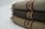Three folded woolen blankets with fringe on the sides and decorative stripes in shades of brown and red.
