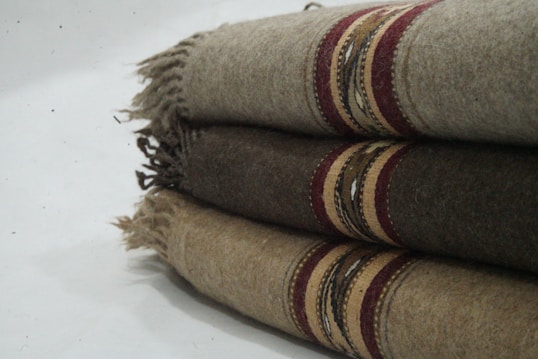 Three folded woolen blankets with fringe on the sides and decorative stripes in shades of brown and red.