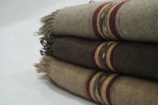 Three folded woolen blankets with fringe on the sides and decorative stripes in shades of brown and red.