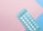 A blister pack containing several small, white pills arranged in rows, placed on a background with pink and blue sections. The packaging seems to be for a form of oral medication, possibly birth control pills.