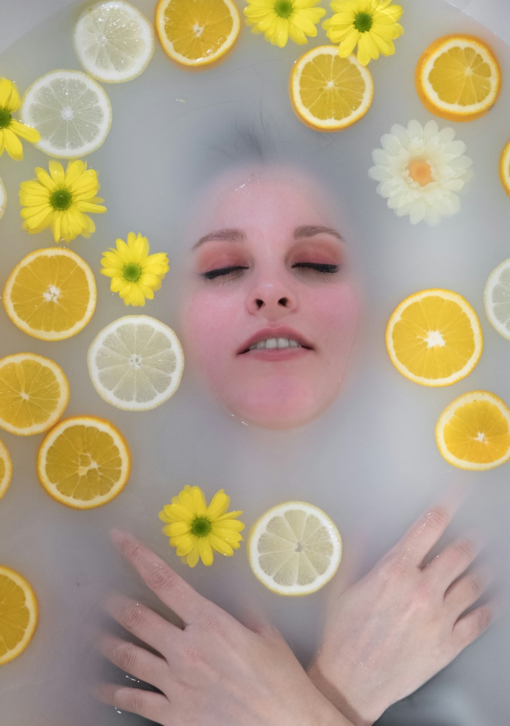 flat-lay photography of woman dipped in water surrounded by yellow lemons and flowers