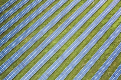 Rows of solar panels are arranged in a diagonal pattern across a green field. The panels are uniformly spaced and cover a large area, emphasizing renewable energy and sustainability.