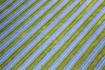 Rows of solar panels are arranged in a diagonal pattern across a green field. The panels are uniformly spaced and cover a large area, emphasizing renewable energy and sustainability.