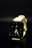 A sleek, modern wristwatch with a black rectangular face and minimalistic design. The watch has a light-colored strap and is set against a dark background, creating a contrast that emphasizes the watch's design.