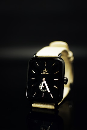 A sleek, modern wristwatch with a black rectangular face and minimalistic design. The watch has a light-colored strap and is set against a dark background, creating a contrast that emphasizes the watch's design.