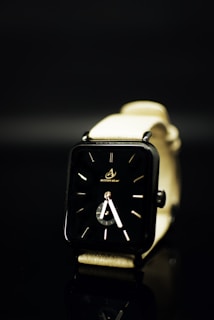 A sleek, modern wristwatch with a black rectangular face and minimalistic design. The watch has a light-colored strap and is set against a dark background, creating a contrast that emphasizes the watch's design.