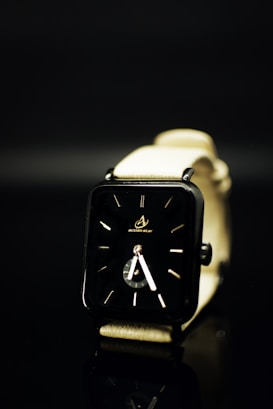 A sleek, modern wristwatch with a black rectangular face and minimalistic design. The watch has a light-colored strap and is set against a dark background, creating a contrast that emphasizes the watch's design.