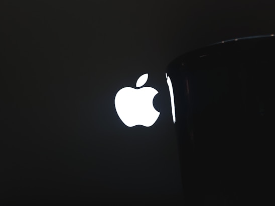 A bright, illuminated logo resembling an apple with a bite taken out of it is prominently displayed against a dark background, partially obscured by an object on the right side.