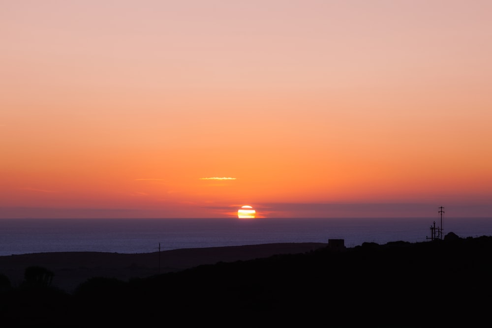 silhouette of hill near body of water during sunset