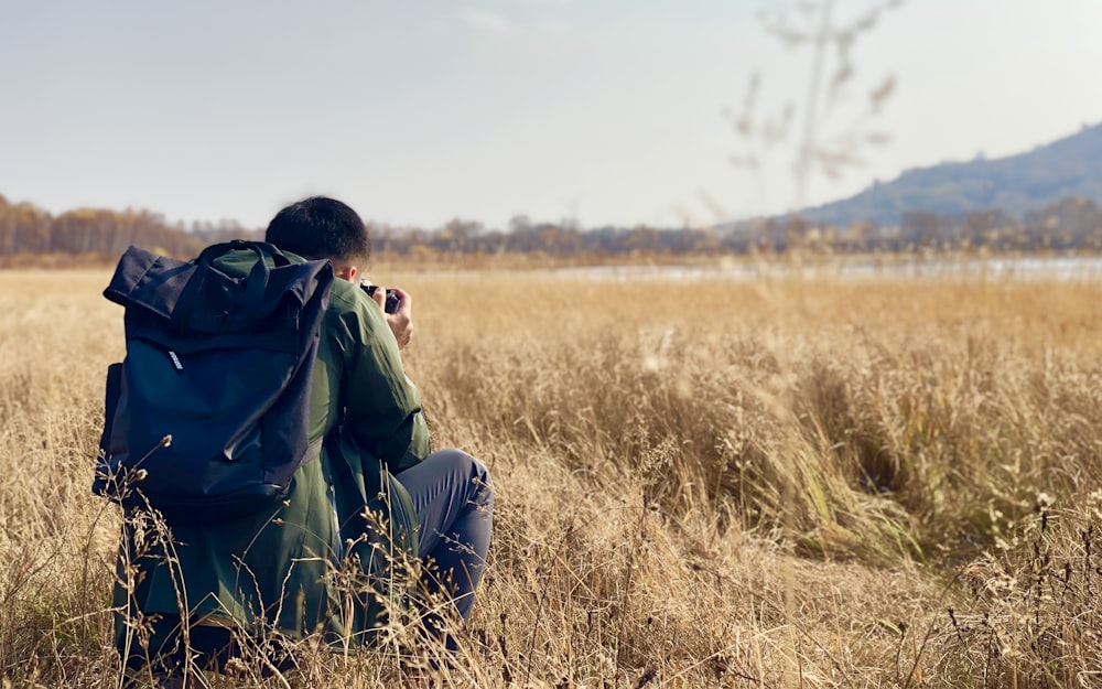 man carrying backpack while taking photo on grassy field