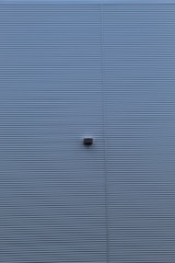 A wall with horizontal corrugated metal panels painted in a muted blue color. A small rectangular light fixture is attached to the center of the wall.