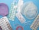 Various contraceptive methods are displayed including birth control pills in blister packs, a diaphragm, a female condom, an intrauterine device (IUD), and an implant. The background is a solid light blue surface.