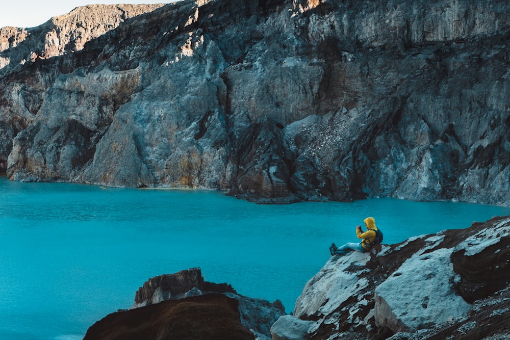 person sitting on rock near body of water