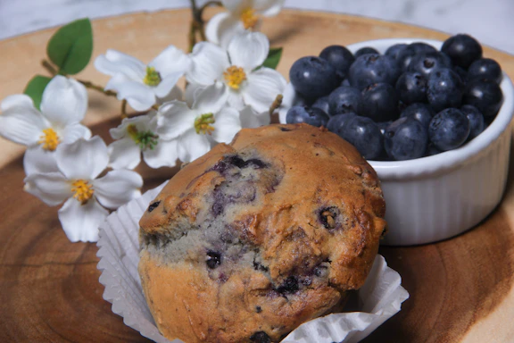 Close-up photo of a lavender muffin topped with edible lavender buds on a rustic wooden table.