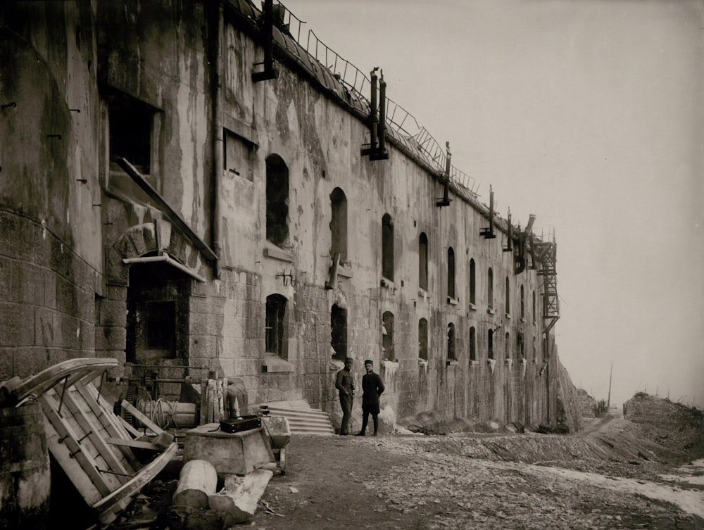fotografia em escala de cinza de dois homens do lado de fora de um edifício de concreto