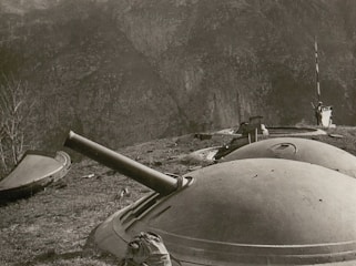 A black and white photograph featuring a series of domed turret-like structures on a rugged hillside. One of the turrets has a protruding gun barrel, indicating a possible artillery installation. The terrain is uneven and appears to be part of a mountainous landscape.