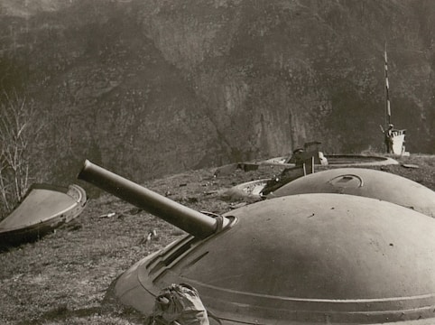 A black and white photograph featuring a series of domed turret-like structures on a rugged hillside. One of the turrets has a protruding gun barrel, indicating a possible artillery installation. The terrain is uneven and appears to be part of a mountainous landscape.