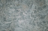 An abstract pattern with interconnected lines and shapes reminiscent of a topographical map. The texture is uneven with a mix of light and dark patches adding depth.