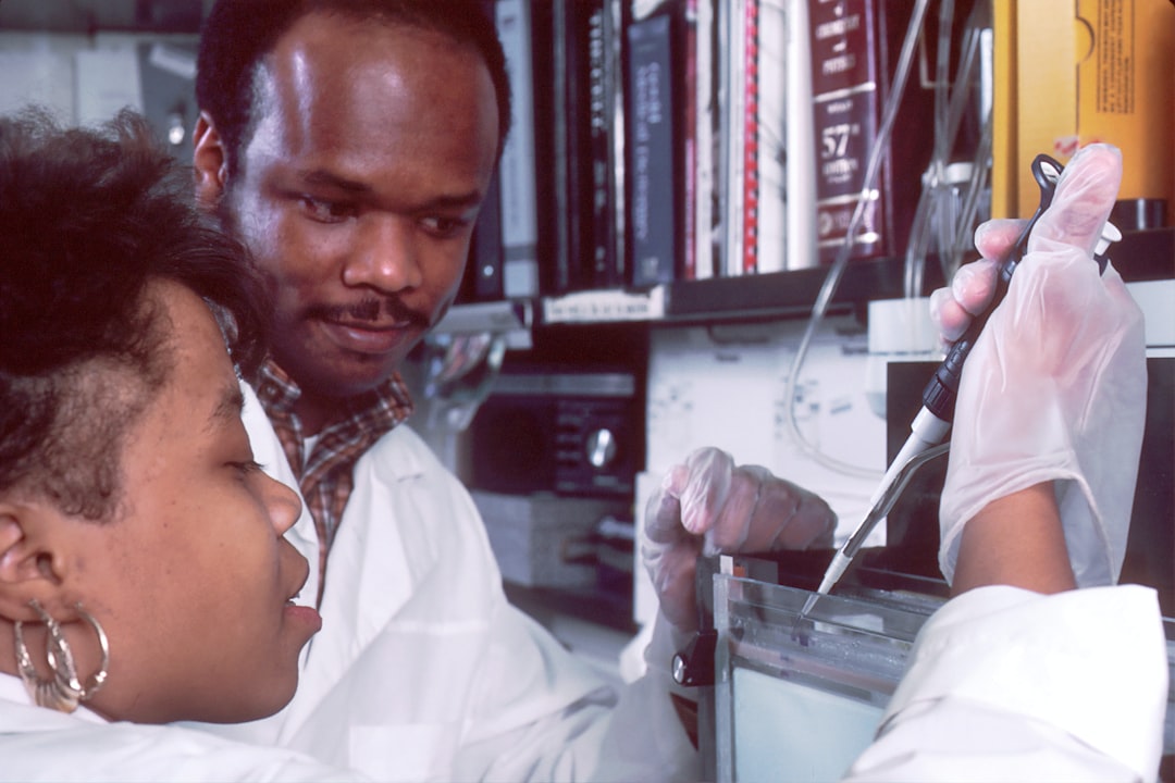 	A Black male scientist is instructing a Black female high school student in the procedure of "southern blotting". Single strands of DNA are transferred onto a nitrocellulose filter, exposed to a radioactive labelled probe, which then sticks, or hybridizes, to a specific DNA sequence. These hybridized sequences will then give off a radioactive signal that can be visualized by exposing the filter to x-ray film, a procedure known as autoradiography.