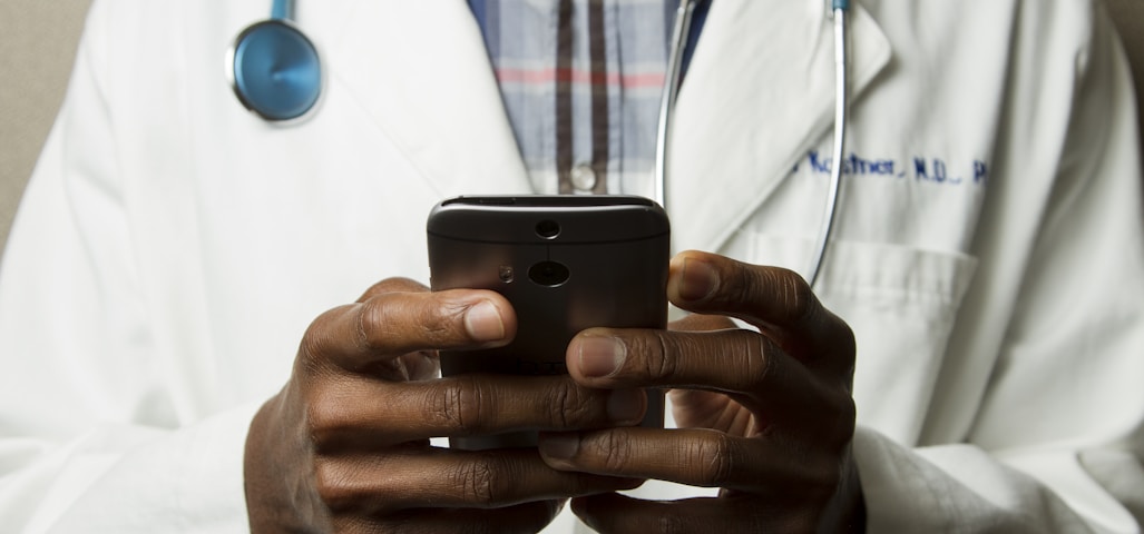 person wearing lavatory gown with green stethoscope on neck using phone while standing