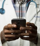 person wearing lavatory gown with green stethoscope on neck using phone while standing