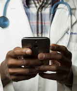 person wearing lavatory gown with green stethoscope on neck using phone while standing