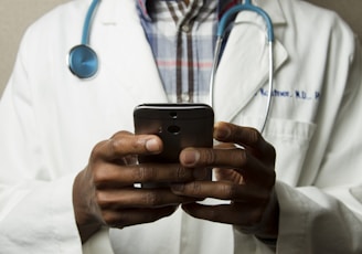 person wearing lavatory gown with green stethoscope on neck using phone while standing