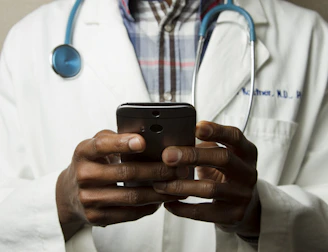 person wearing lavatory gown with green stethoscope on neck using phone while standing