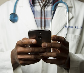 person wearing lavatory gown with green stethoscope on neck using phone while standing