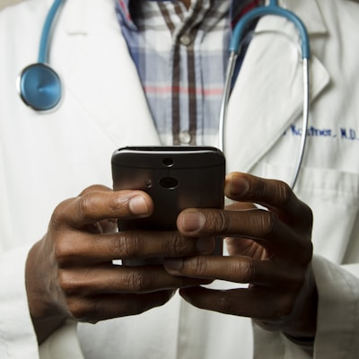 person wearing lavatory gown with green stethoscope on neck using phone while standing