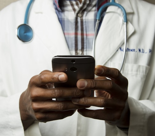 person wearing lavatory gown with green stethoscope on neck using phone while standing