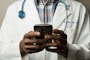 person wearing lavatory gown with green stethoscope on neck using phone while standing