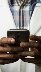 person wearing lavatory gown with green stethoscope on neck using phone while standing