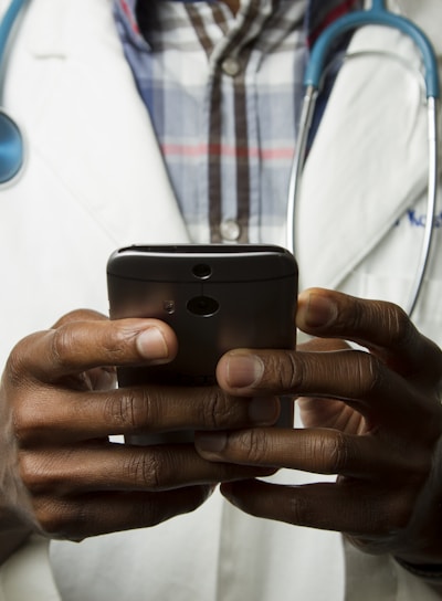 person wearing lavatory gown with green stethoscope on neck using phone while standing