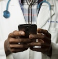 person wearing lavatory gown with green stethoscope on neck using phone while standing