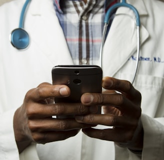 person wearing lavatory gown with green stethoscope on neck using phone while standing