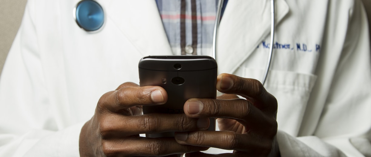 person wearing lavatory gown with green stethoscope on neck using phone while standing