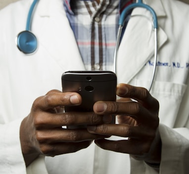 person wearing lavatory gown with green stethoscope on neck using phone while standing