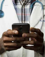 person wearing lavatory gown with green stethoscope on neck using phone while standing