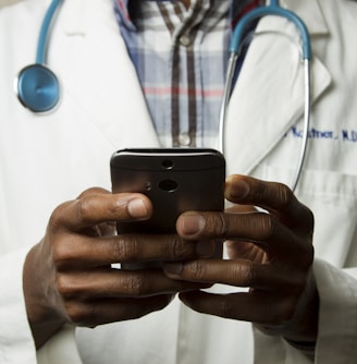 person wearing lavatory gown with green stethoscope on neck using phone while standing