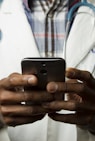 person wearing lavatory gown with green stethoscope on neck using phone while standing