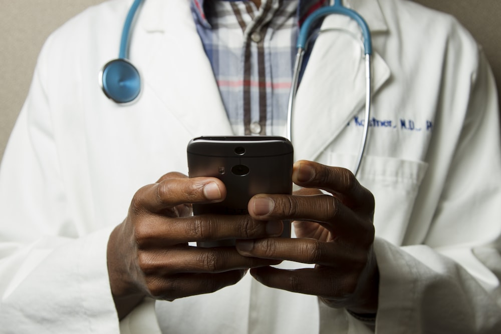 personne portant une blouse de toilette avec un stéthoscope vert sur le cou en utilisant un téléphone en position debout