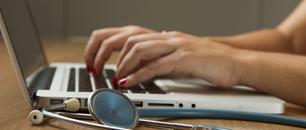 person sitting while using laptop computer and green stethoscope near