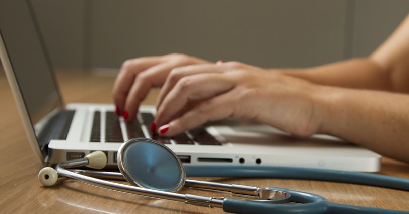 person sitting while using laptop computer and green stethoscope near