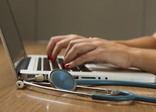 person sitting while using laptop computer and green stethoscope near