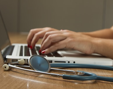 person sitting while using laptop computer and green stethoscope near