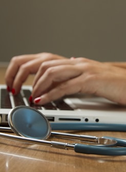 person sitting while using laptop computer and green stethoscope near