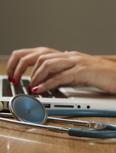 person sitting while using laptop computer and green stethoscope near