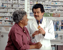 A pharmacist in a white coat showing a pill bottle to a woman